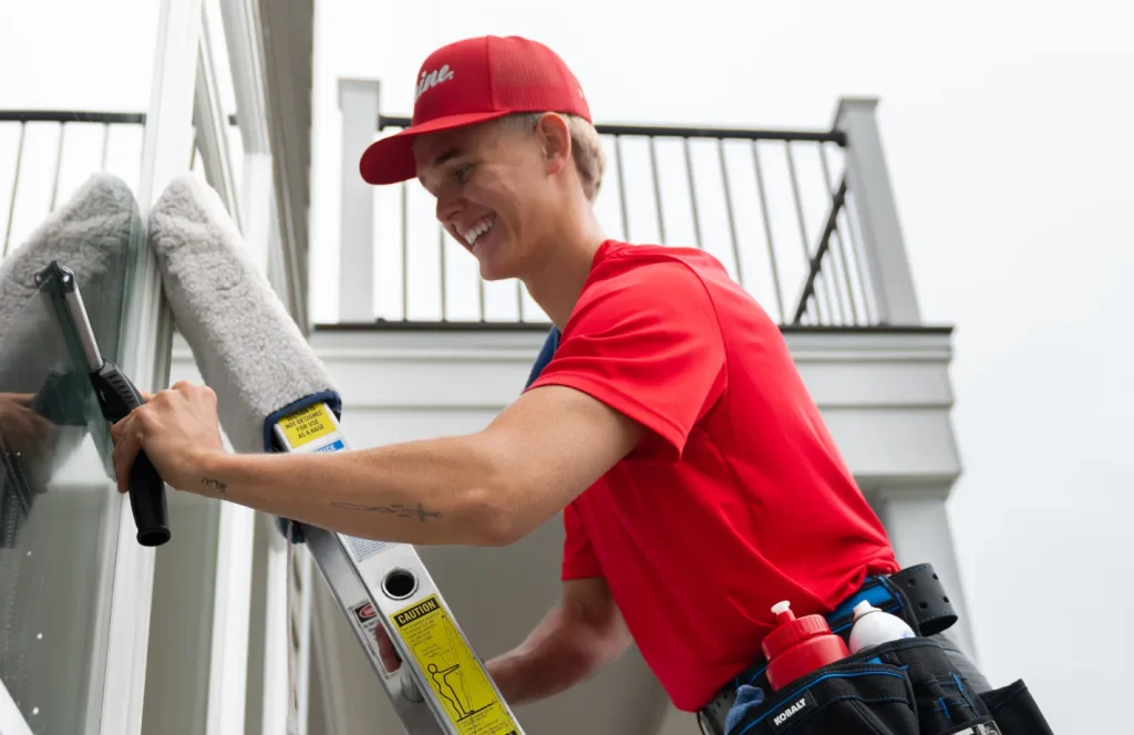 Shine technician cleaning exterior windows while working on a ladder.