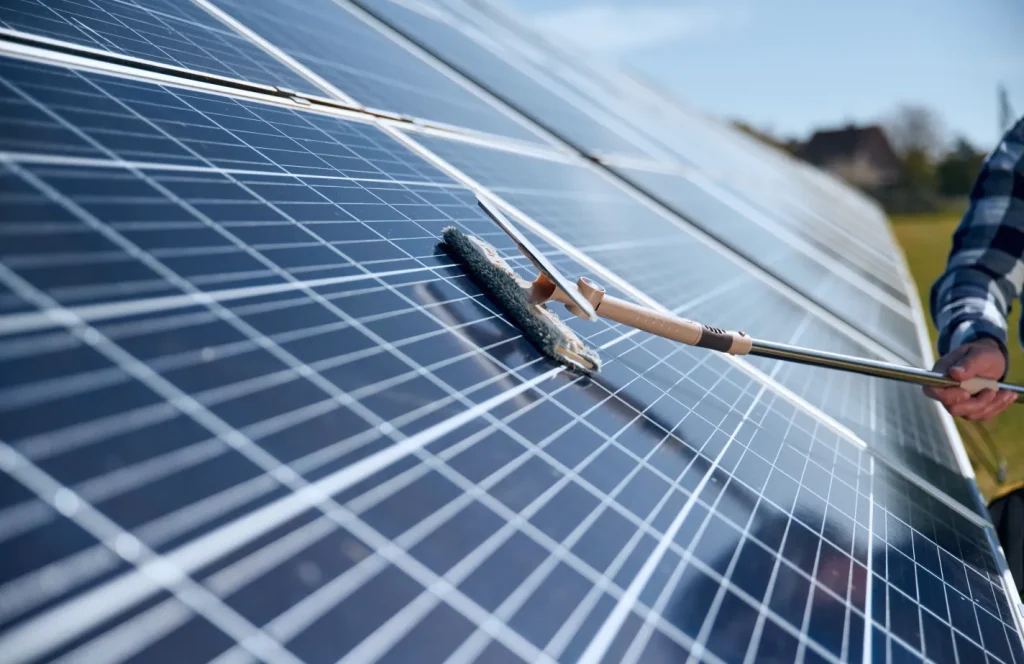 Worker cleaning solar panels with a long-handled brush.