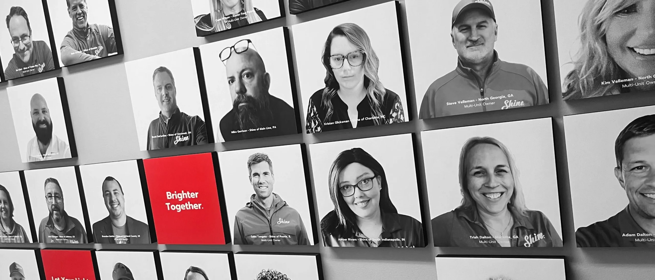 Wall display featuring portraits of Shine Franchise team members and owners.